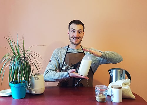 Man in apron showing home-made oat milk between his hands.