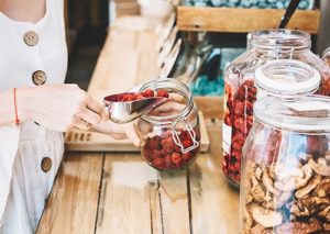 Women scooping out dry strawberries from a glass jar in a bulk shop.