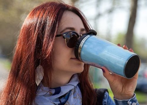 Girl drinking a cup of coffee with a reusable cup.