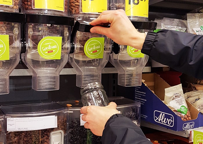 Man serving nuts from a bulk dispenser in a glass jar.