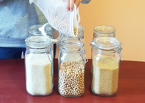 Girl transferring chickpeas from bags to a storage container in a shelf.