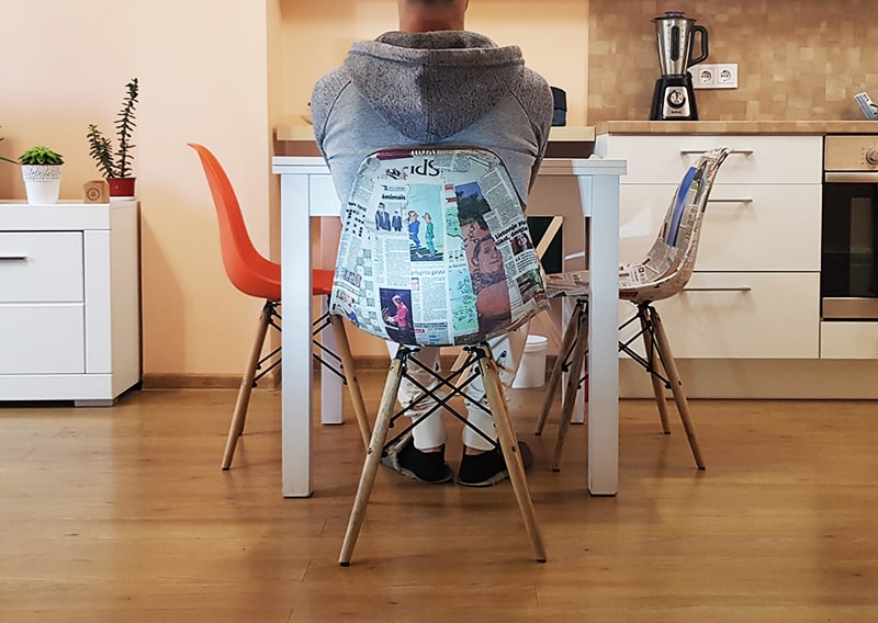 Man sitting on a chair refurbished with recycled newspaper.