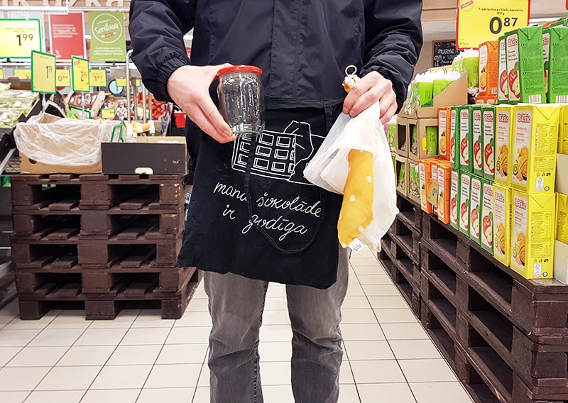 Man holding glass jar and cloth bags in grocery store