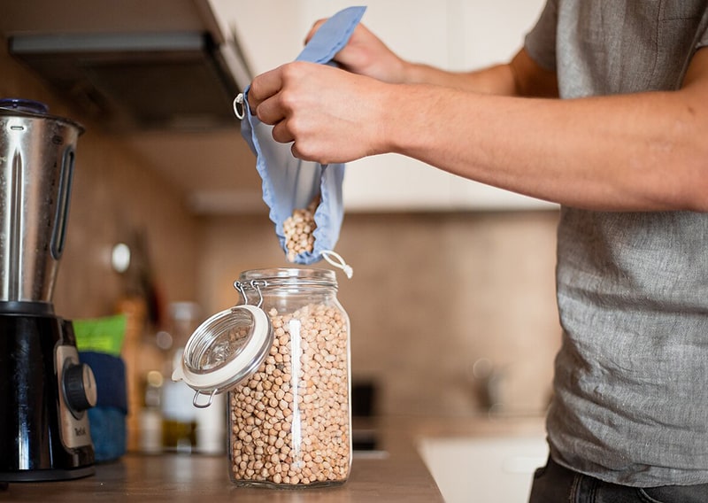 person filling up glass jar with bulk food
