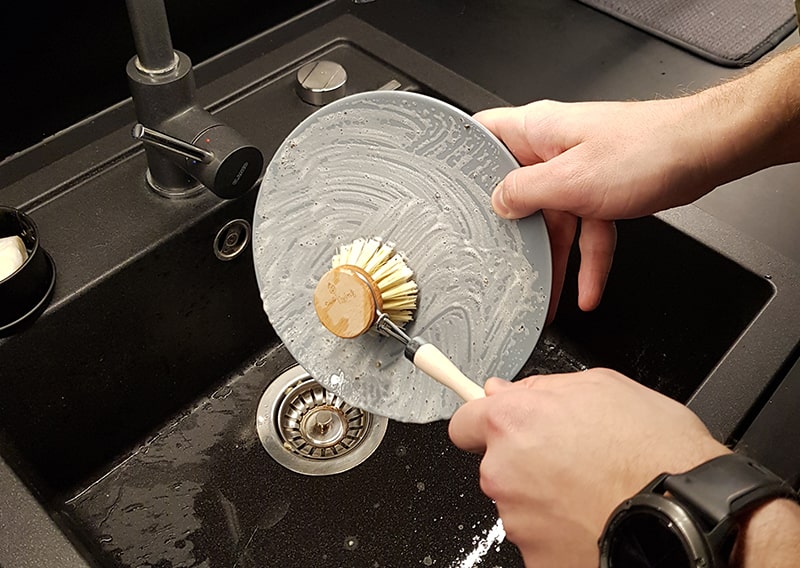 Person using a wooden brush to scrub a plate over the sink